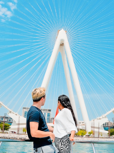 Couple on yacht with view of Ain Dubai Ferris wheel at Dubai Harbour.