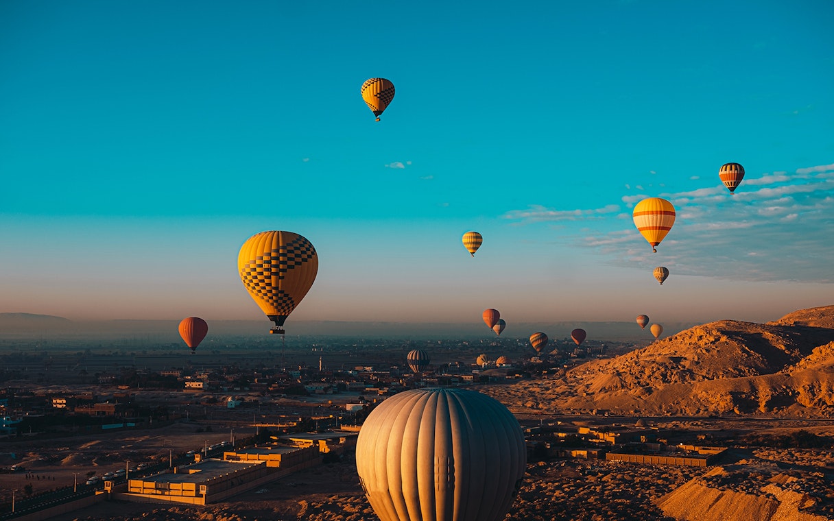 Hot air balloons over desert landscape during Nile cruise from Aswan to Luxor.