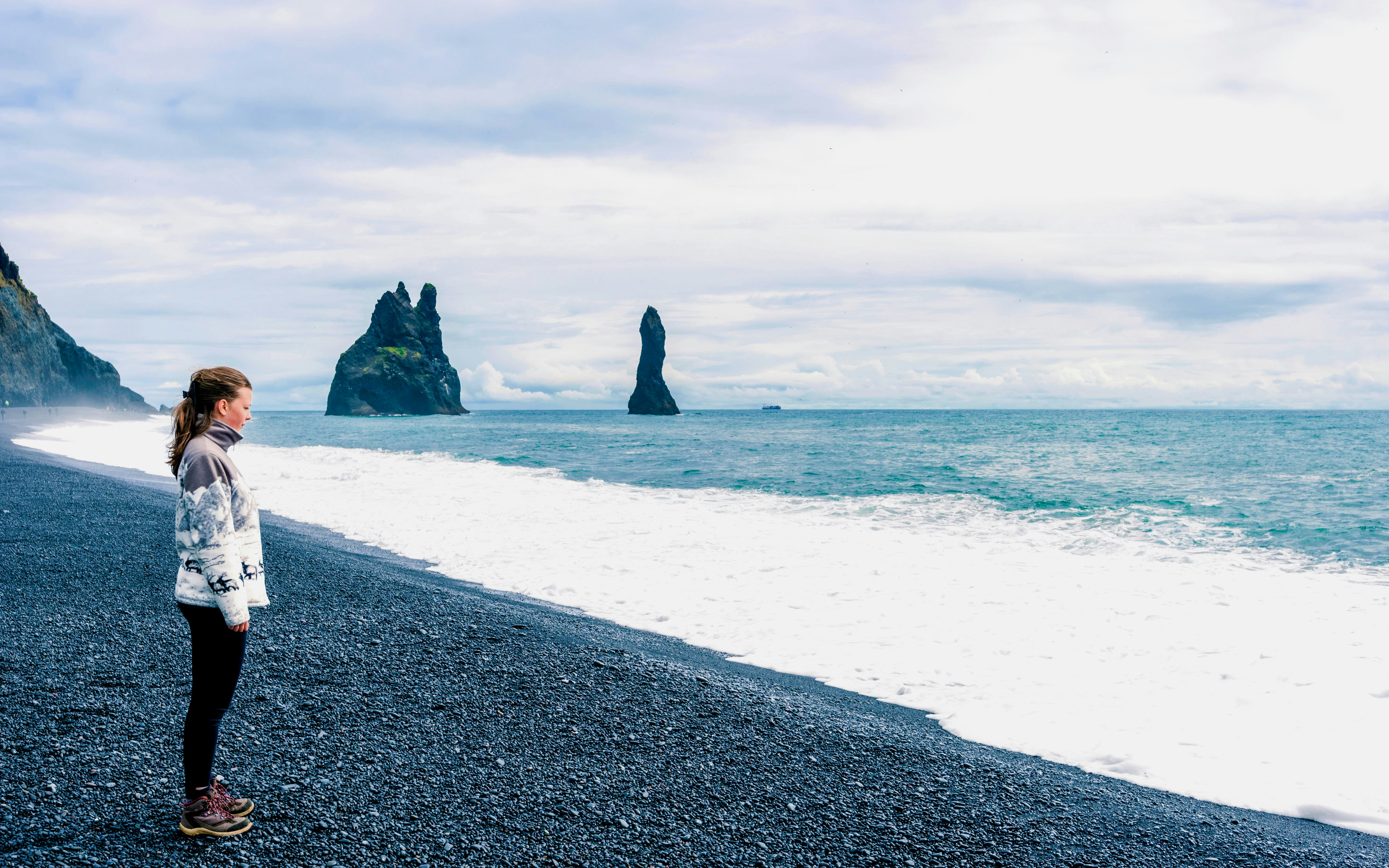 Person standing on Reynisfjara Black Sand Beach with sea stacks in the background.