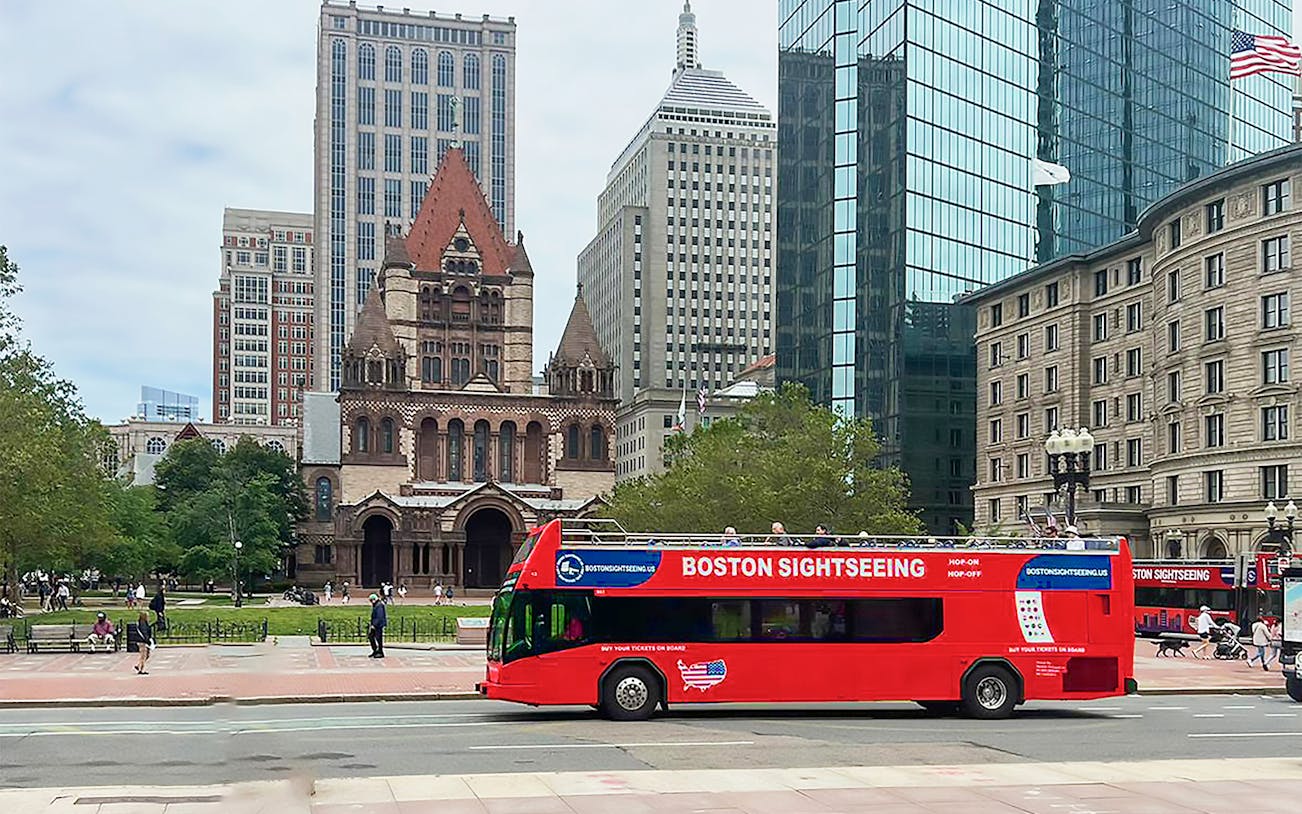 Boston sightseeing bus near Trinity Church with city buildings in the background.