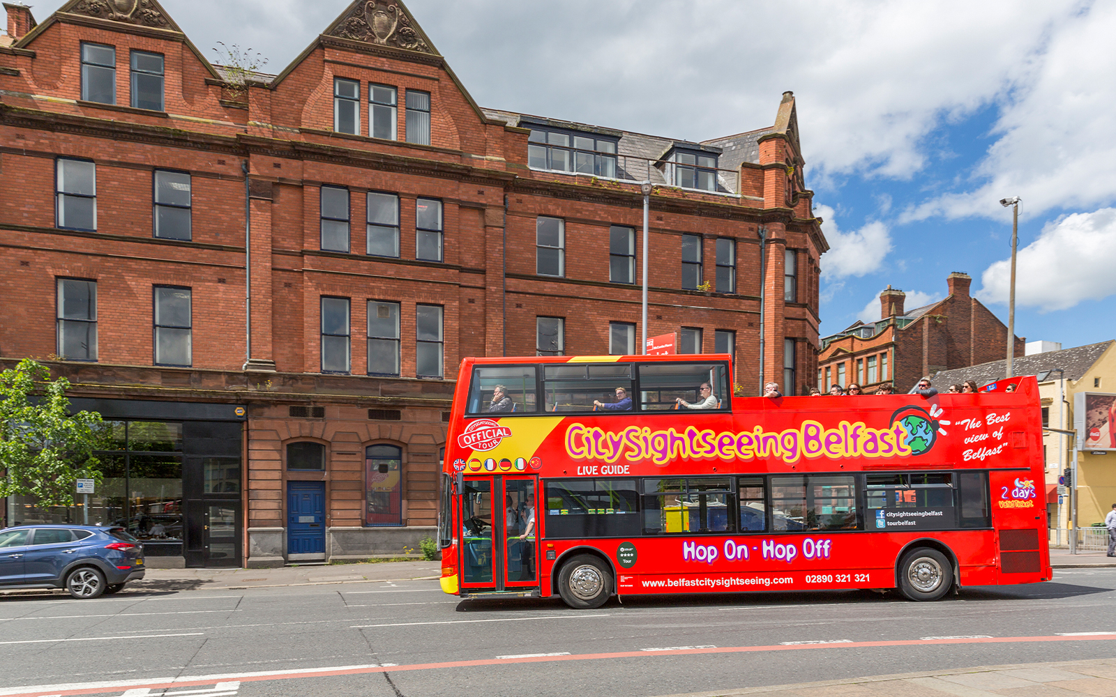 Belfast city tour bus passing by a historic brick building near The Bakery.