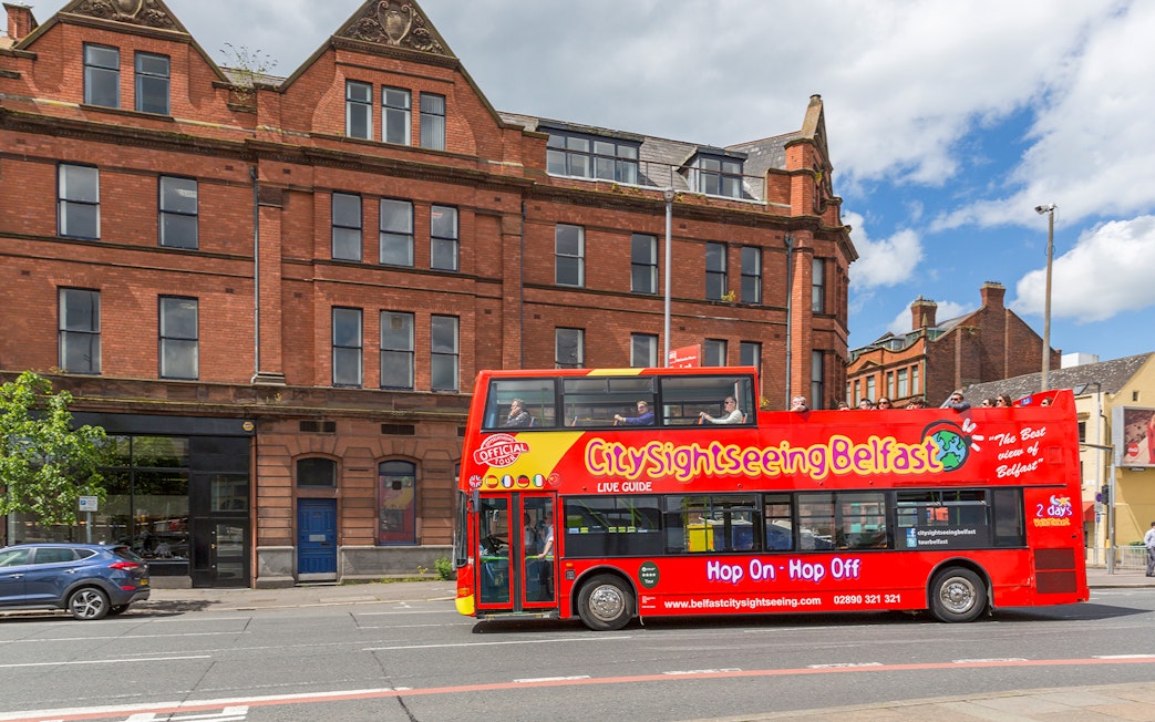 Belfast city tour bus passing by a historic brick building near The Bakery.