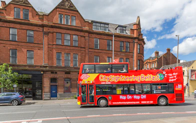 Belfast city tour bus passing by a historic brick building near The Bakery.