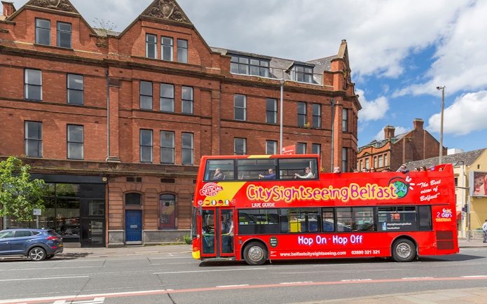 Belfast city tour bus passing by a historic brick building near The Bakery.