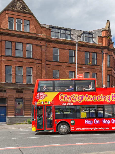 Belfast city tour bus passing by a historic brick building near The Bakery.