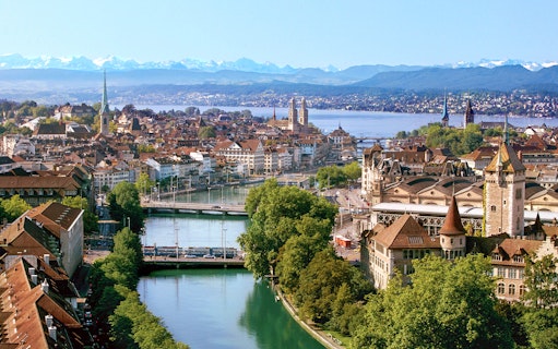 Zurich cityscape with Limmat River, historic buildings, and distant Alps.