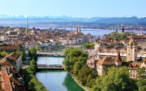 Zurich cityscape with Limmat River, historic buildings, and distant Alps.