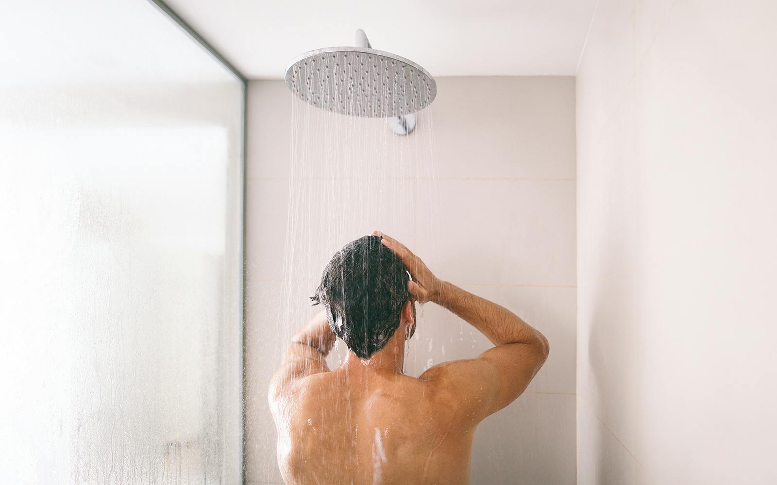 Man taking a shower with water streaming from overhead showerhead.