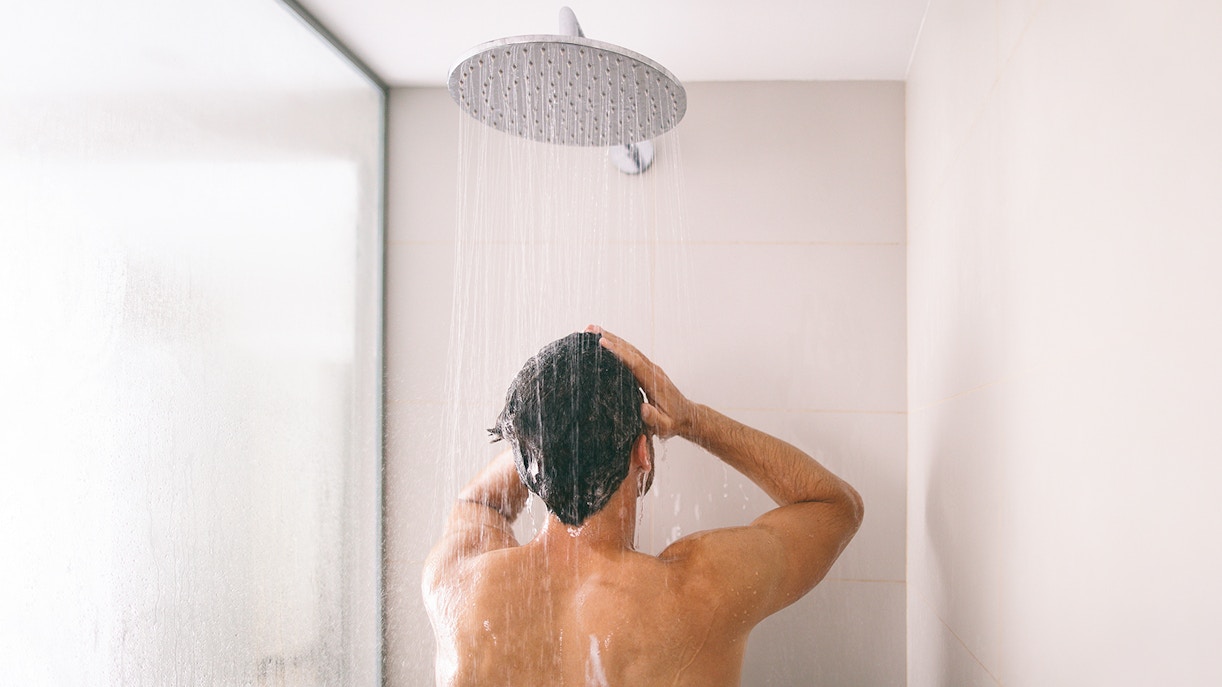 Man taking a shower with water streaming from overhead showerhead.