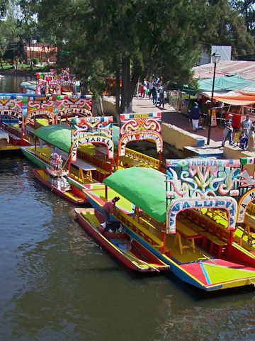 Colorful trajineras on Xochimilco canal with people boarding.