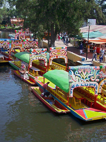 Colorful trajineras on Xochimilco canal with people boarding.