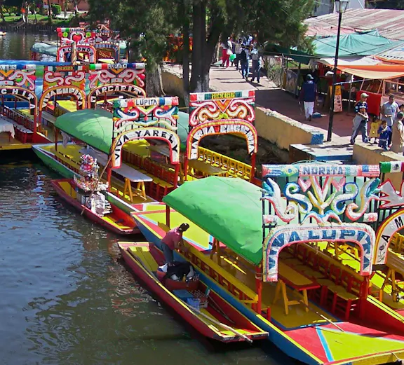 Colorful trajineras on Xochimilco canal with people boarding.