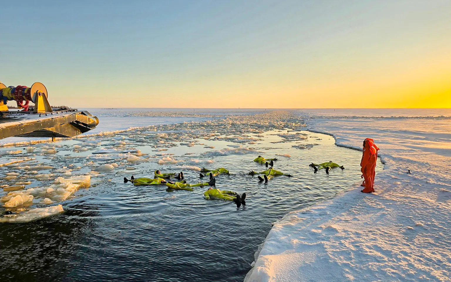 Participants in survival suits floating near Icebreaker Sampo during morning cruise in frozen sea.