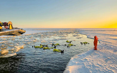 Participants in survival suits floating near Icebreaker Sampo during morning cruise in frozen sea.
