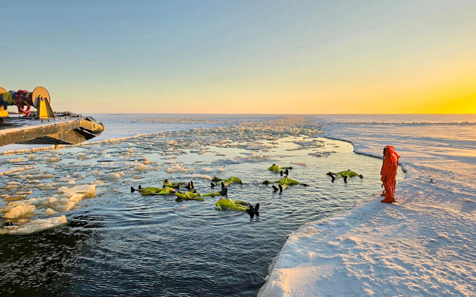 Participants in survival suits floating near Icebreaker Sampo during morning cruise in frozen sea.