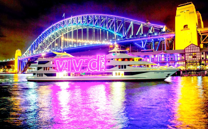 Sydney Harbour Bridge illuminated during Vivid Sydney light show with cruise ship in foreground.