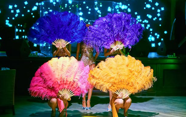 Cabaret dancers performing with colorful feather fans on stage.