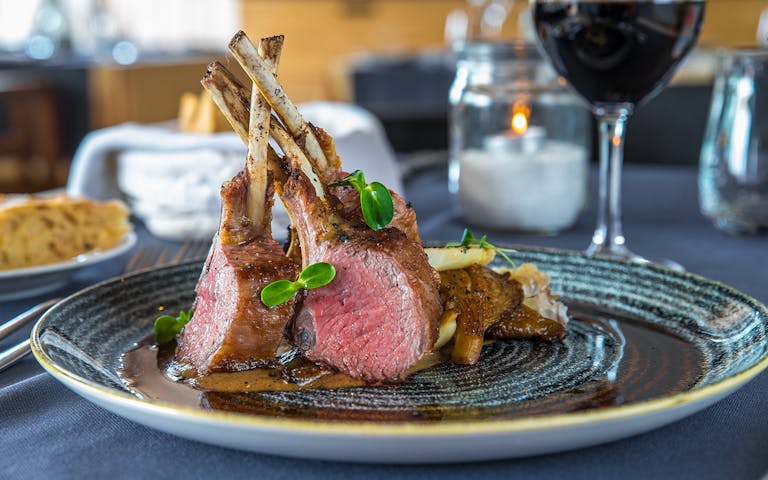 Crispy lamb ribs served on a wooden board with herbs and dipping sauce.