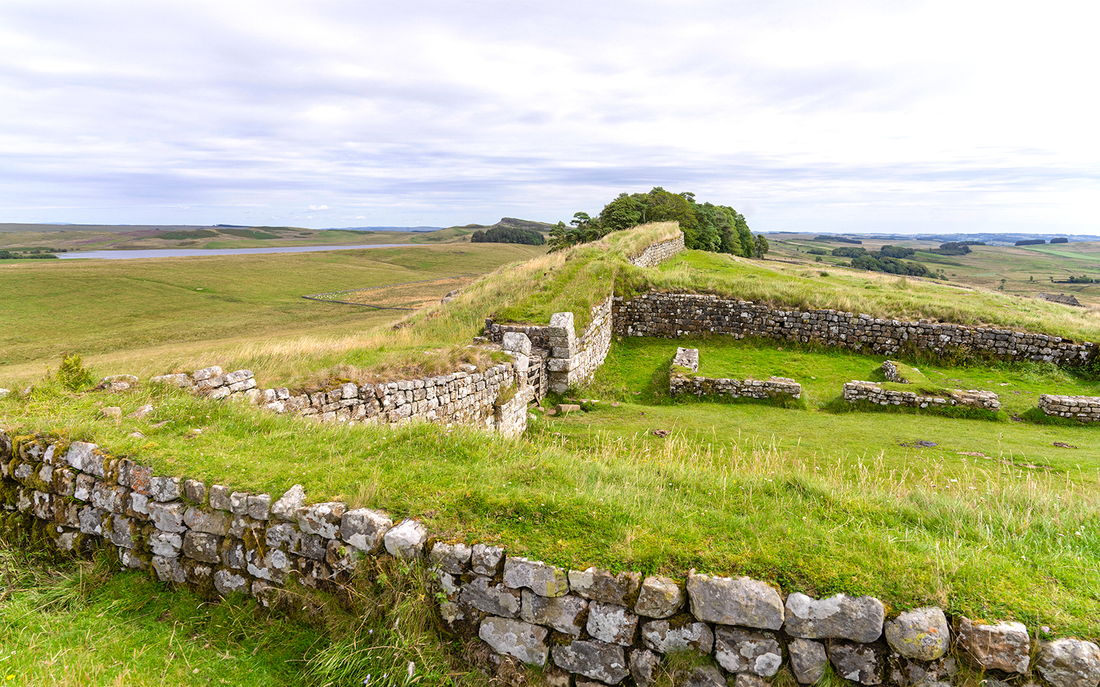 Housesteads Roman Fort ruins with stone walls and green landscape in Northumberland, England.