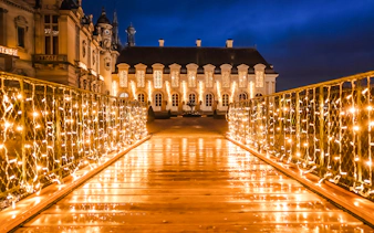 Chateau of Chantilly illuminated at night with festive lights on a bridge.