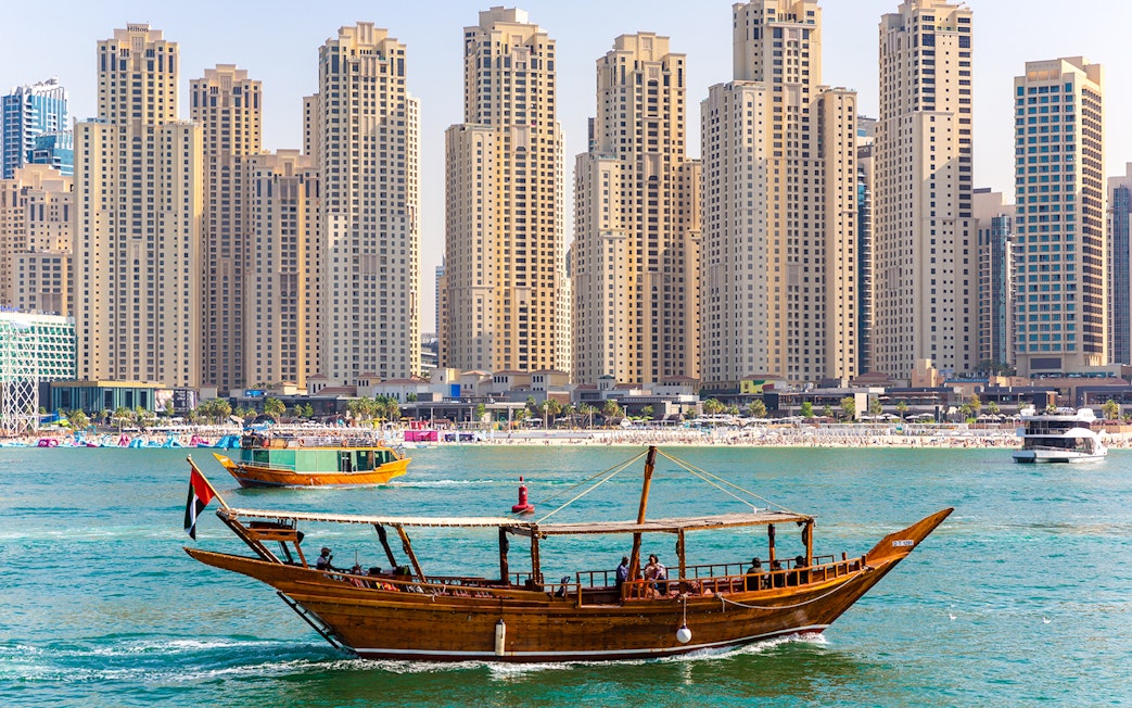 Traditional dhow boat sailing in front of Dubai Marina skyscrapers.