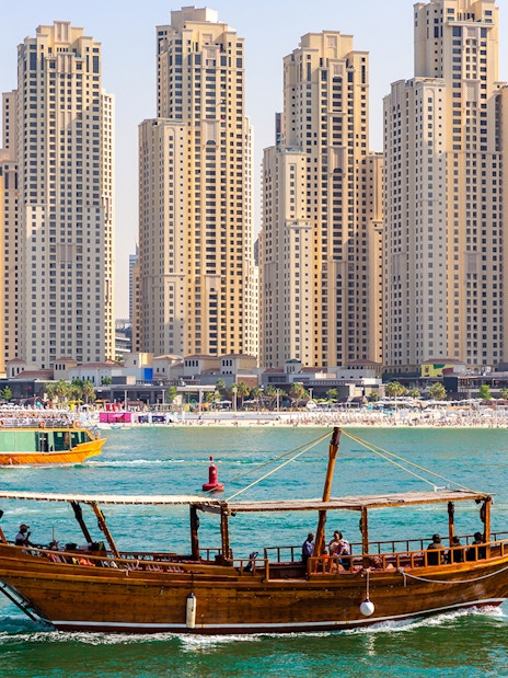 Traditional dhow boat sailing in front of Dubai Marina skyscrapers.