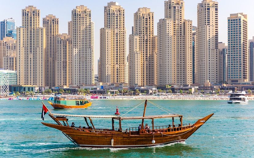 Traditional dhow boat sailing in front of Dubai Marina skyscrapers.