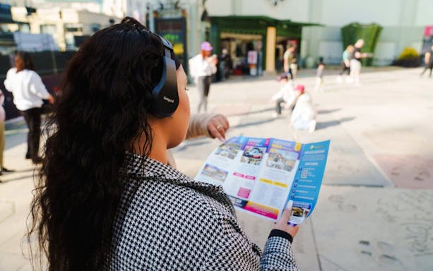 Guest using audio guide on Hollywood Walk of Fame tour, holding a brochure.