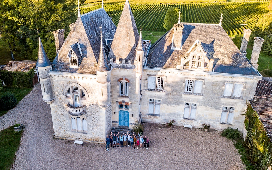 Saint-Emilion chateau with group of tourists in courtyard, surrounded by vineyards.