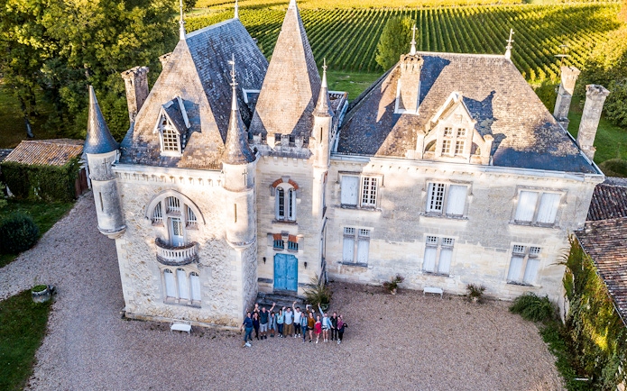 Saint-Emilion chateau with group of tourists in courtyard, surrounded by vineyards.