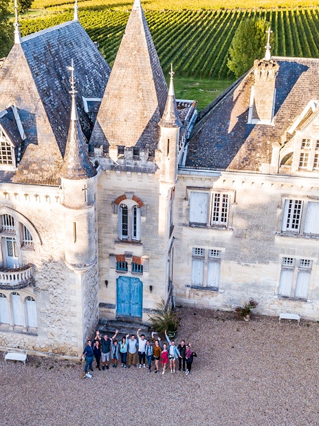 Saint-Emilion chateau with group of tourists in courtyard, surrounded by vineyards.