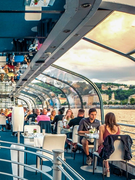 Budapest dinner cruise with guests dining under a glass roof on the Danube River.