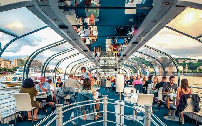 Budapest dinner cruise with guests dining under a glass roof on the Danube River.