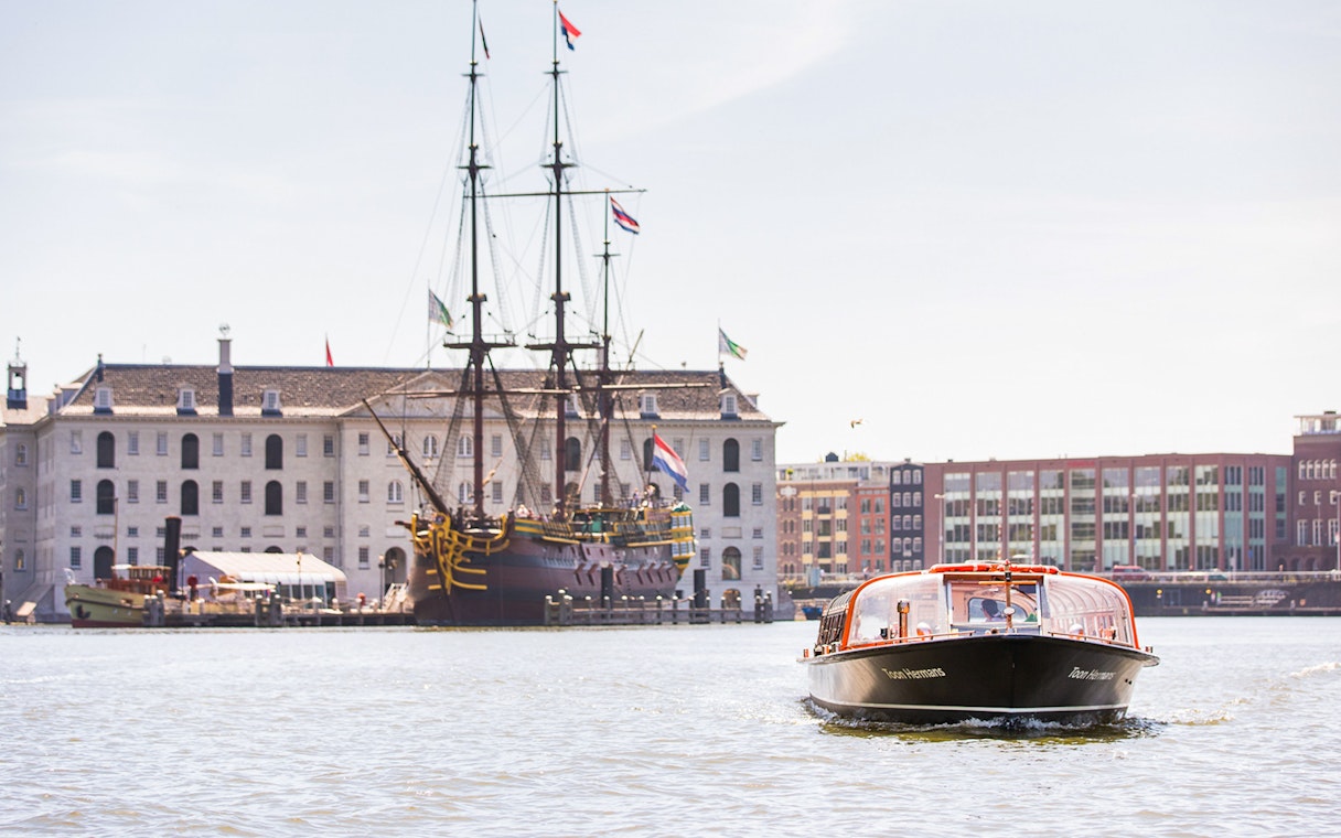 Amsterdam canal boat near the National Maritime Museum with historic ship in view.
