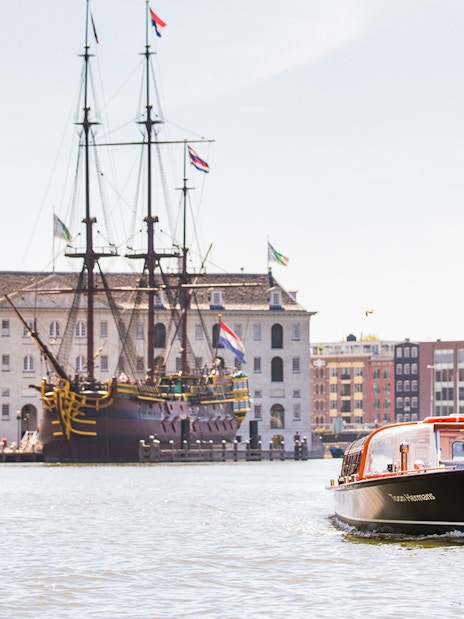 Amsterdam canal boat near the National Maritime Museum with historic ship in view.