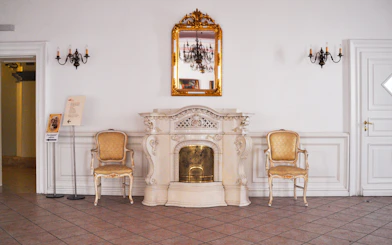 Gödöllő Royal Palace interior with ornate fireplace and chairs.