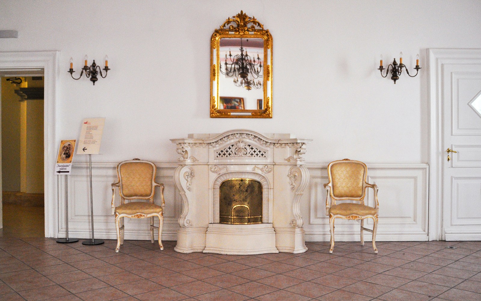 Gödöllő Royal Palace interior with ornate fireplace and chairs.