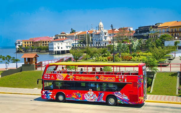 Red double-decker bus on Hop On Hop Off tour in Panama City with historic buildings in the background.
