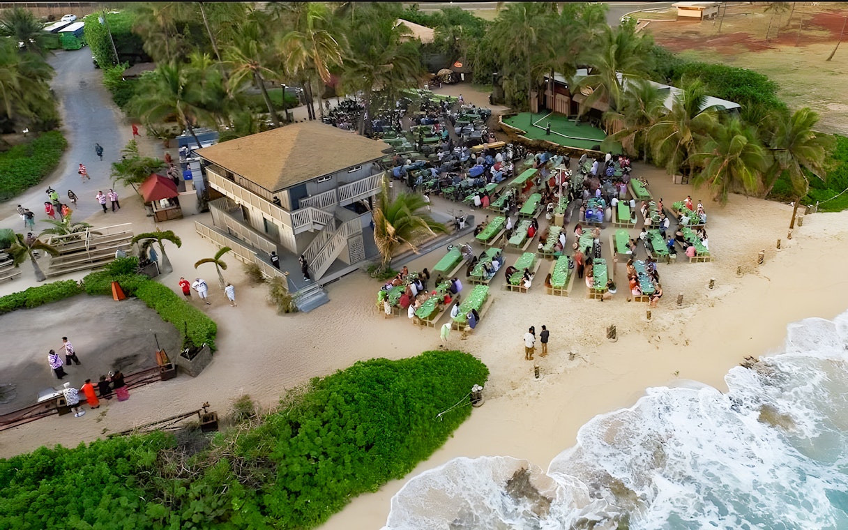 Drone view of Germaine's Luau with guests seated near the shore in Oahu, Hawaii.