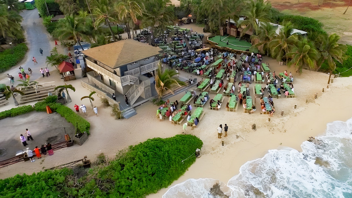 Drone view of Germaine's Luau with guests seated near the shore in Oahu, Hawaii.