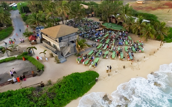 Drone view of Germaine's Luau with guests seated near the shore in Oahu, Hawaii.