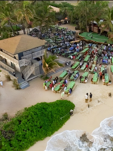 Drone view of Germaine's Luau with guests seated near the shore in Oahu, Hawaii.