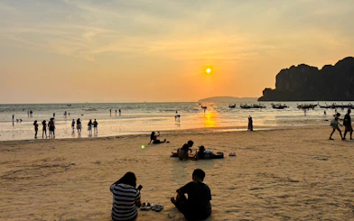 Sunset view at Railay Beach, Krabi with people relaxing on the sand and boats in the water.