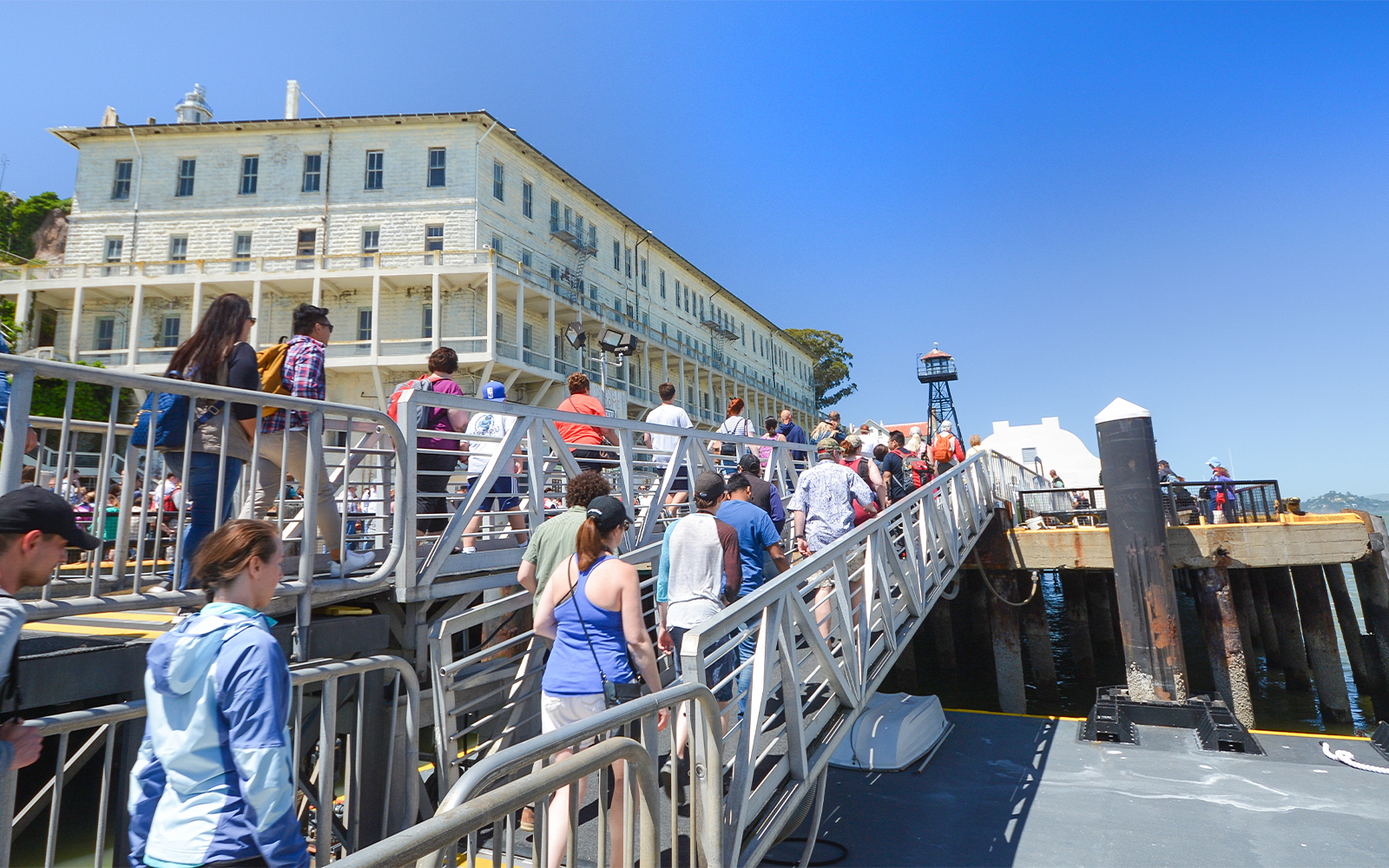 Visitors walking up a ramp to Alcatraz Island, San Francisco, with historic buildings in view.