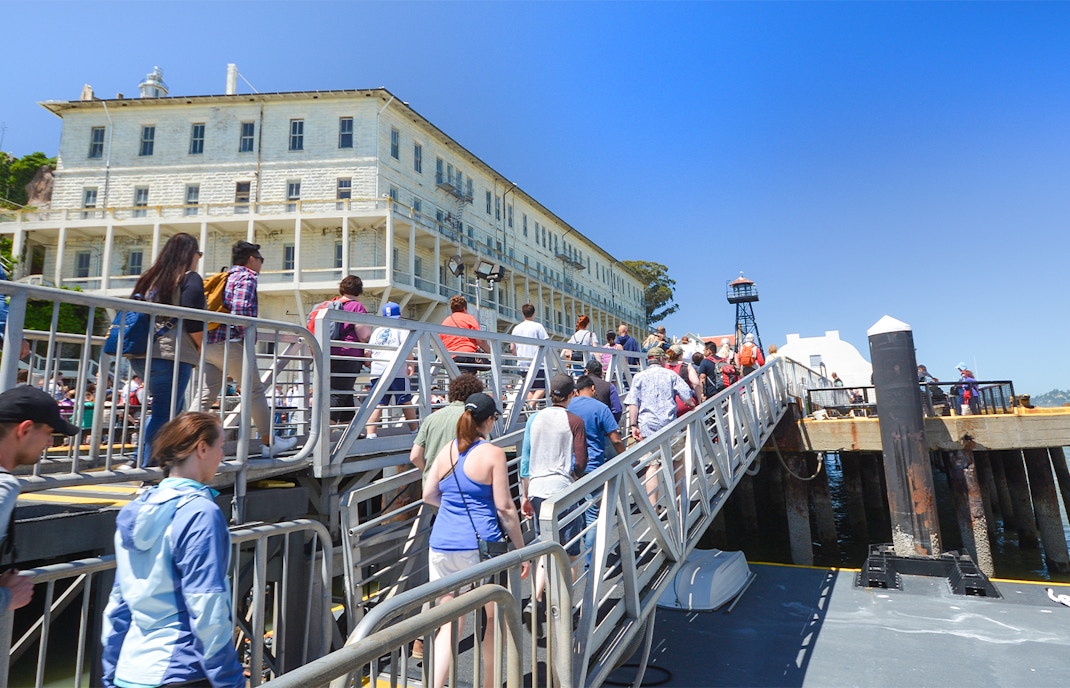 Visitors walking up a ramp to Alcatraz Island, San Francisco, with historic buildings in view.