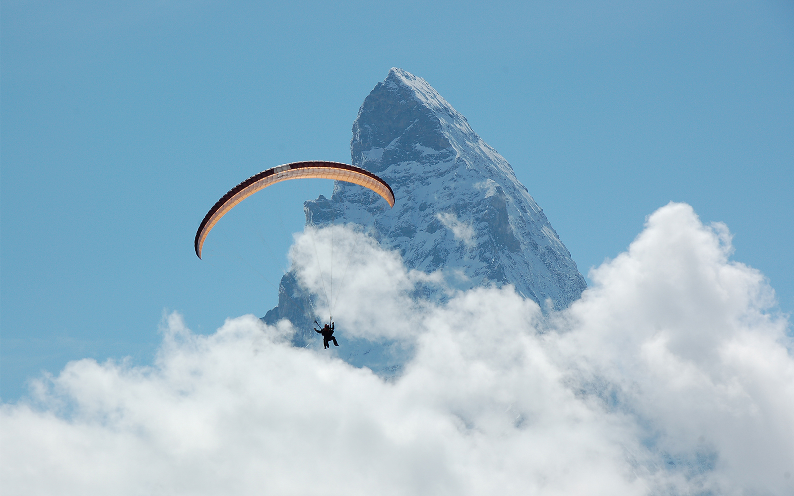Paraglider soaring near Matterhorn Peak, Gornergrat, surrounded by clouds.