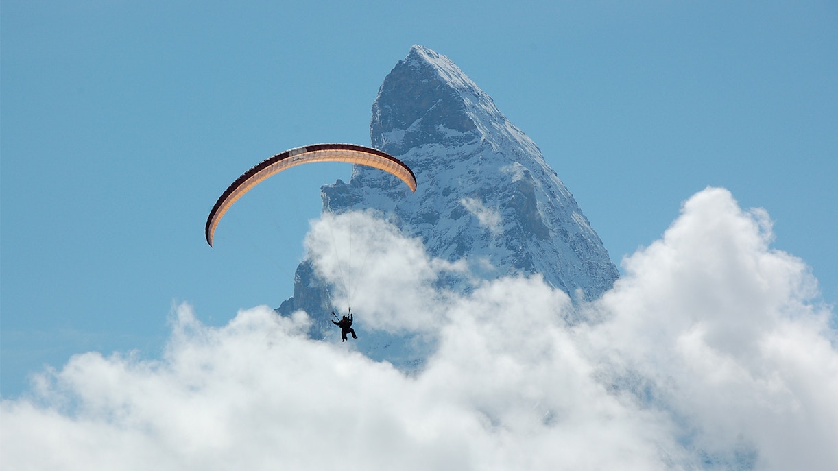 Paraglider soaring near Matterhorn Peak, Gornergrat, surrounded by clouds.