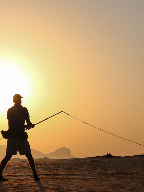 Person flying a falcon at sunrise in the desert during a safari.