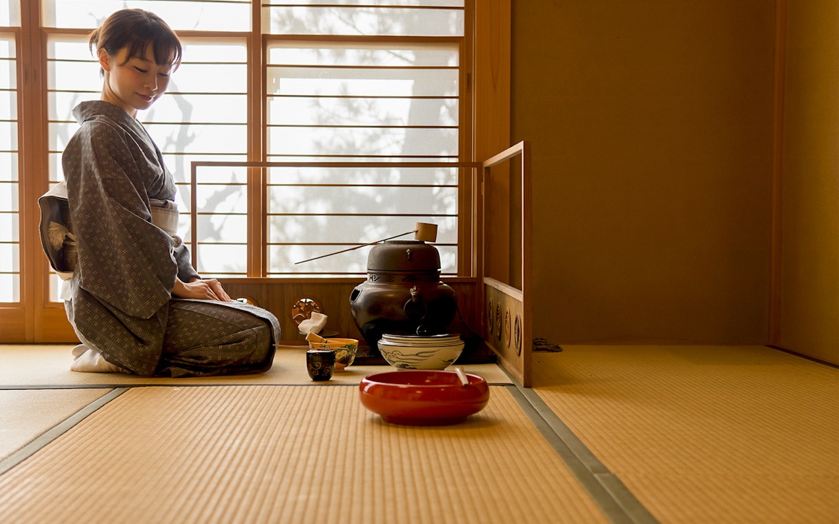 Tea ceremony in Kyoto with a woman in kimono preparing tea on tatami mats.