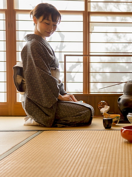 Tea ceremony in Kyoto with a woman in kimono preparing tea on tatami mats.